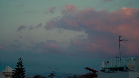 Un-Impresionante-Movimiento-De-Nubes-Durante-La-Puesta-De-Sol-Sobre-Los-Tejados-De-Los-Edificios,-Pájaros-Volando-Y-Un-Avión,-Cielo-Colorido,-Medio-Oriente,-Tel-Aviv-Israel,-Vídeo-Sony-4k