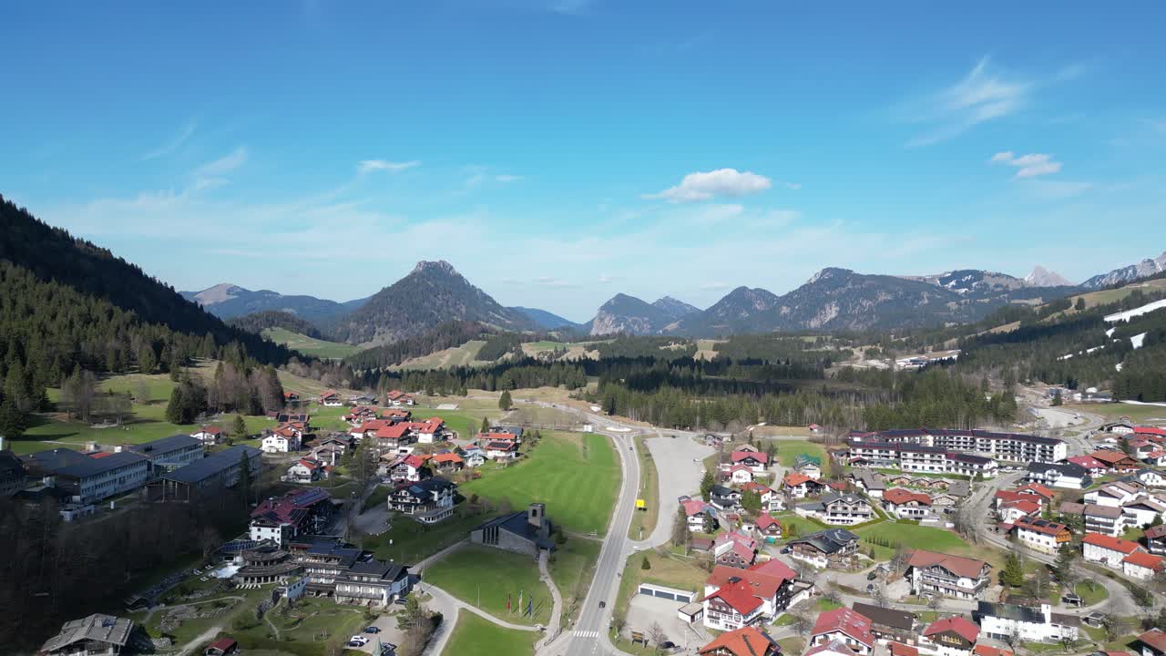 Drone view of Oberjoch in the Bavarian Alps showing snow patches, green meadows, and forested hills. A peaceful mountain village perfect for nature and travel visuals.