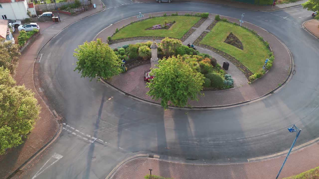 Small war memorial in Sheringham roundabout, framed by trees and garden paths