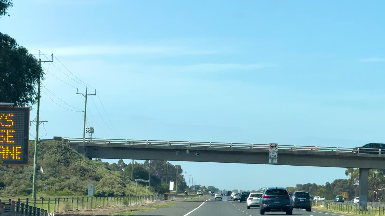 Cars travel along a sunny highway beneath a bridge on Great Ocean Road, Victoria, Australia. Clear skies and open road create a serene atmosphere