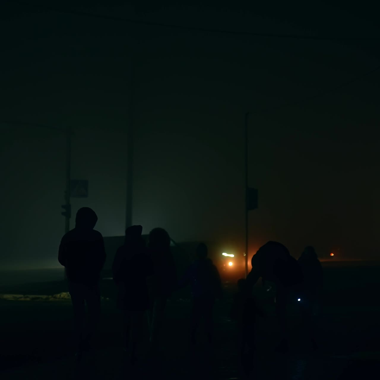 Human silhouettes moving by the dark city streets during blackout. People using flashlights to see the way and let the drivers know about them