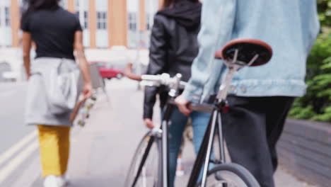 rear view of female friends with skateboards and bike walking through city street