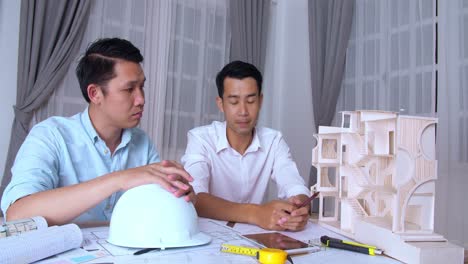 two asian male architects working with new architectural house model