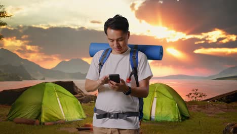 man using phone while camping at sunset