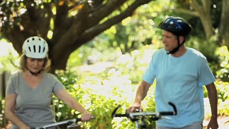 Pareja-Mayor-Caminando-Y-Empujando-Bicicletas