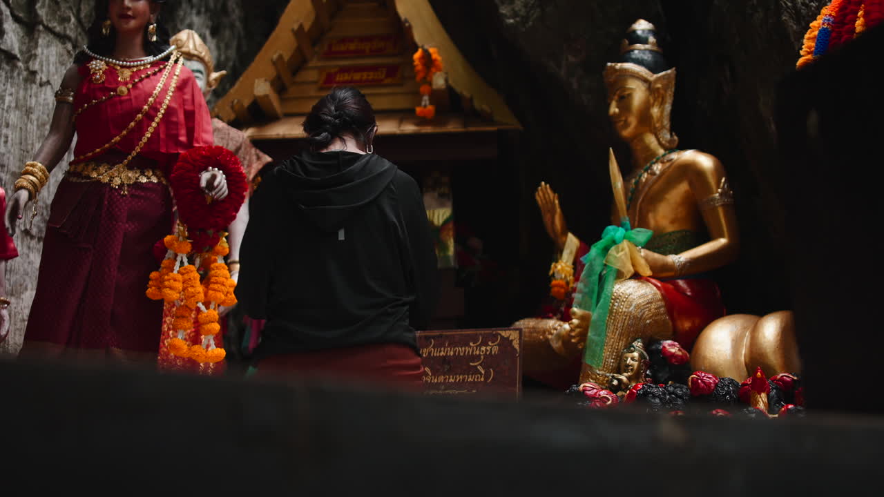Woman Praying at Cave Temple with Golden Statues