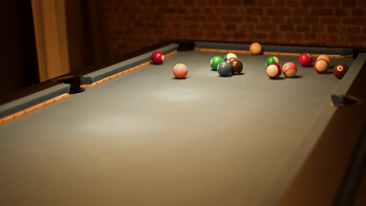 Les boules de billard se dispersent après le coup d’ouverture sur une table de billard verte, éclairage intérieur chaleureux, mur de briques