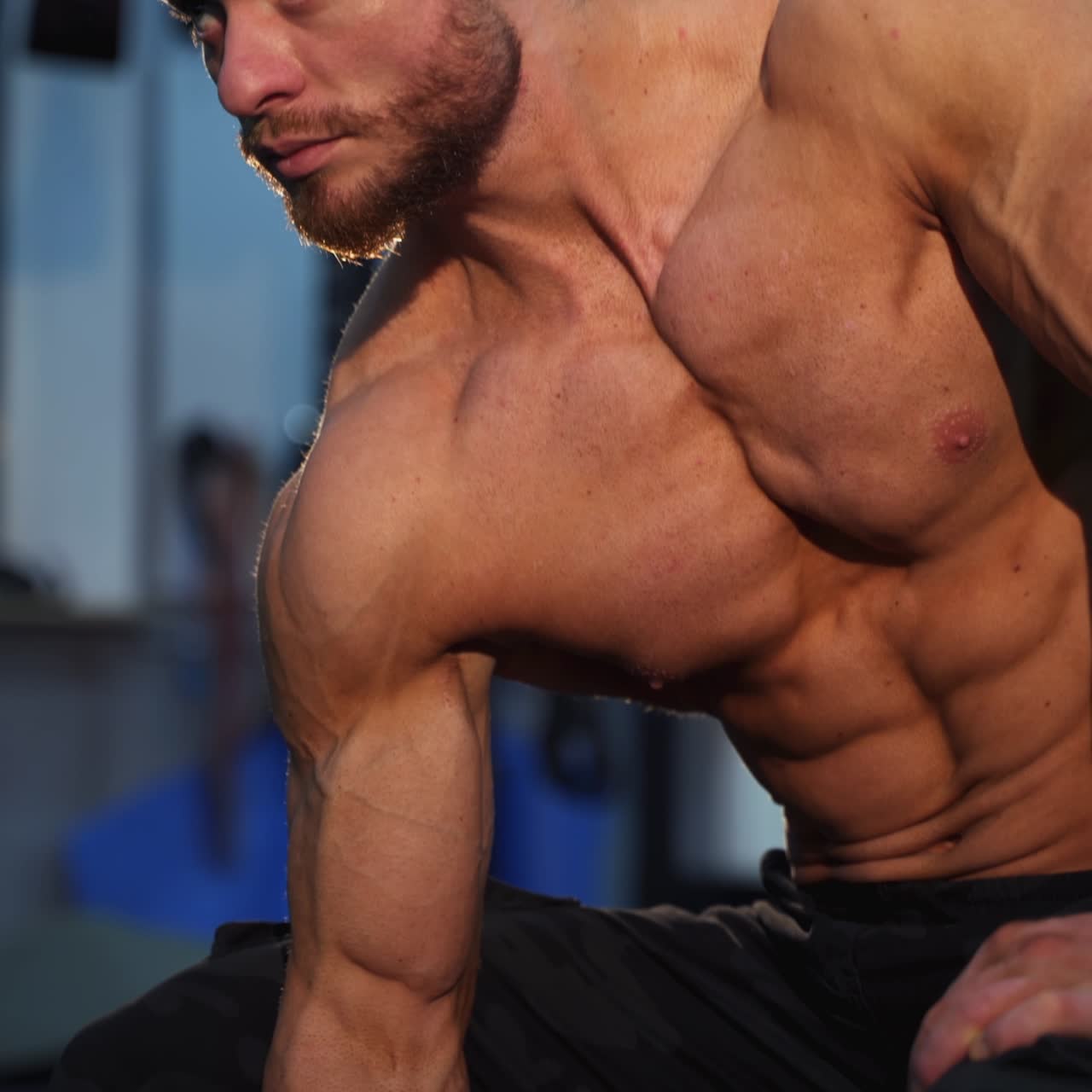 Fitness guy training indoors. Shirtless bodybuilder lifting heavy dumbbell. Muscular athlete exercising with a dumbbell in gym. Close-up
