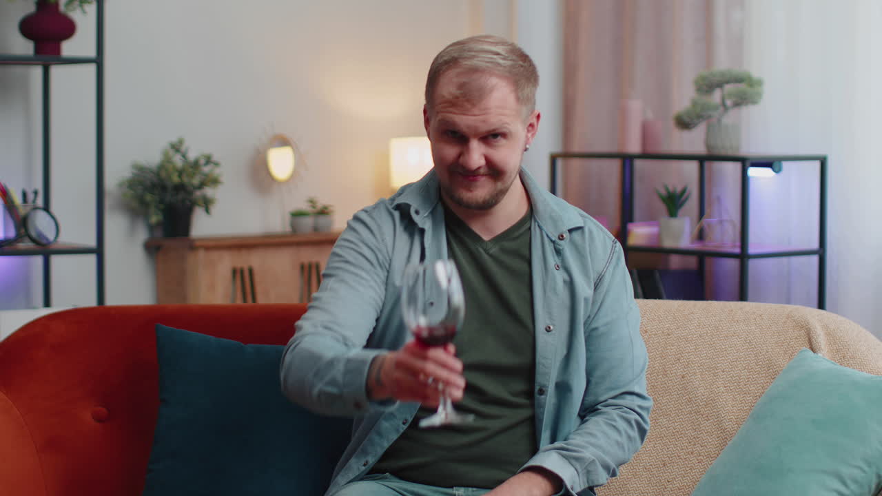 joven adulto feliz bebiendo un vaso de vino rojo celebrando el aniversario de cumpleaños ganando la lotería en casa