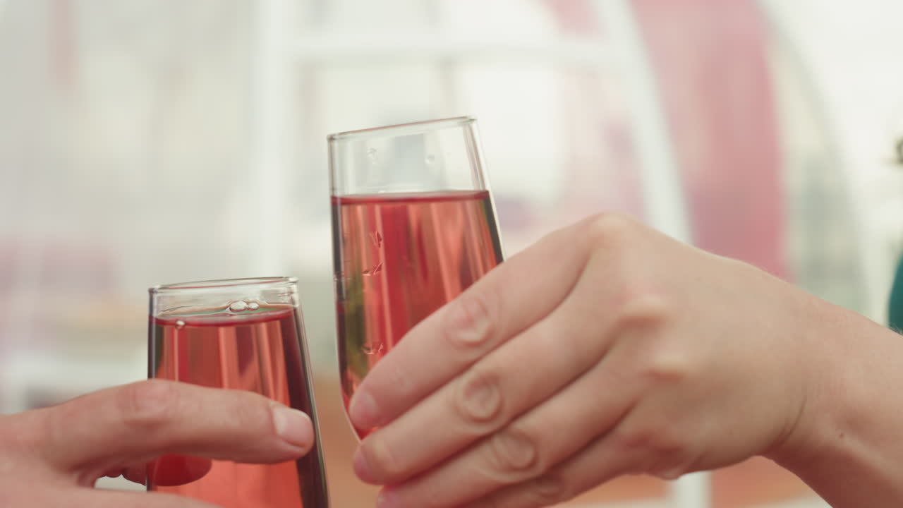 mesa en la azotea, rosas, vasos, pareja caucásica compartiendo un brindis íntimo sobre un mantel rojo con una bandeja de fruta, cesta de mimbre, granada y uvas; hombre con traje oscuro y mujer con vestido verde intercambiando