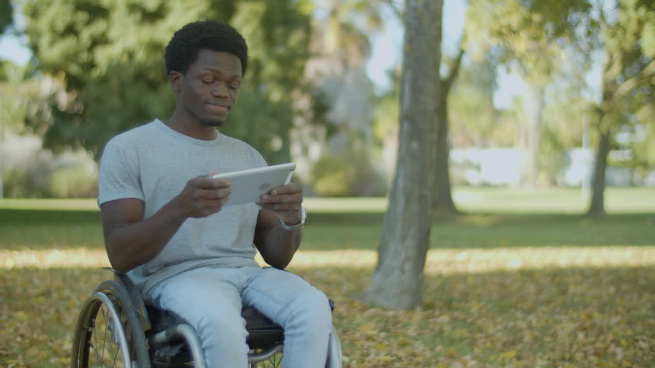 Young Black Man In Wheelchair Spending Time Outdoors With Tablet