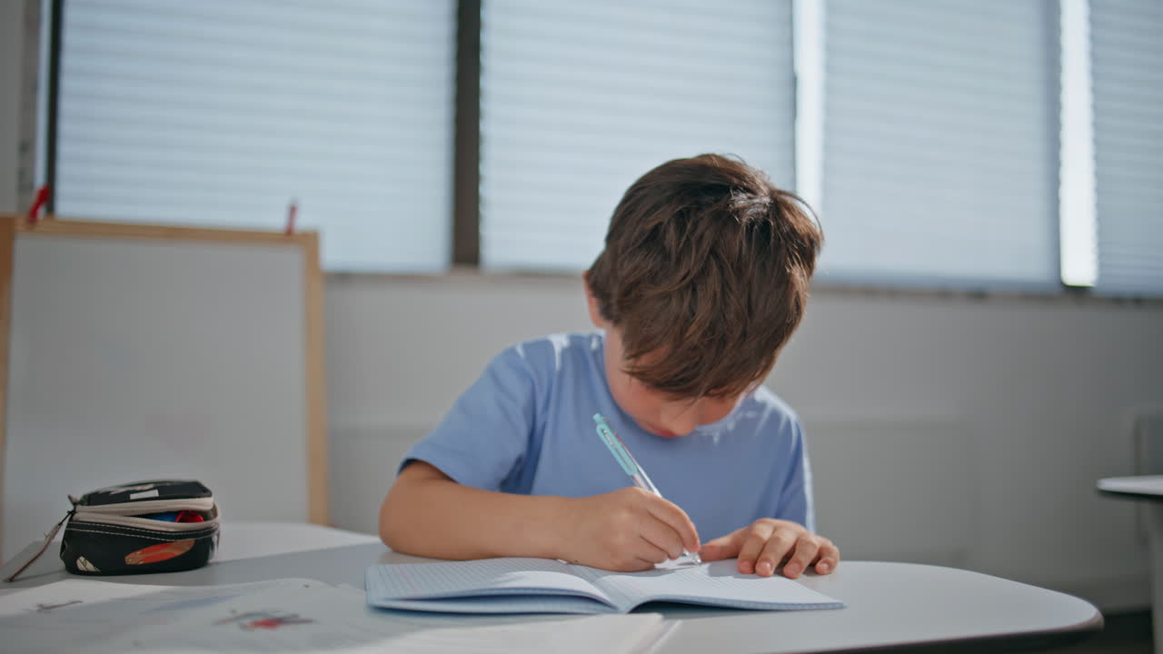 Thoughtful schoolboy holding pen thinking in classroom closeup. Boy writing