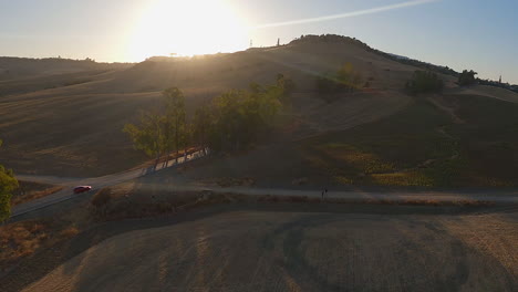 Aerial:-Car-drives-toward-golden-sunrise-on-tree-lined-country-road