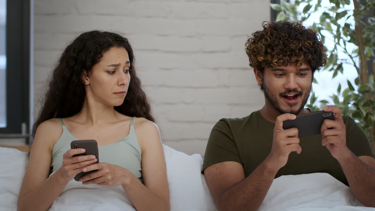 Couple in Bed, One Focused on Phone