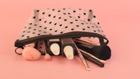 makeup bag with brushes and cosmetics on a pink background