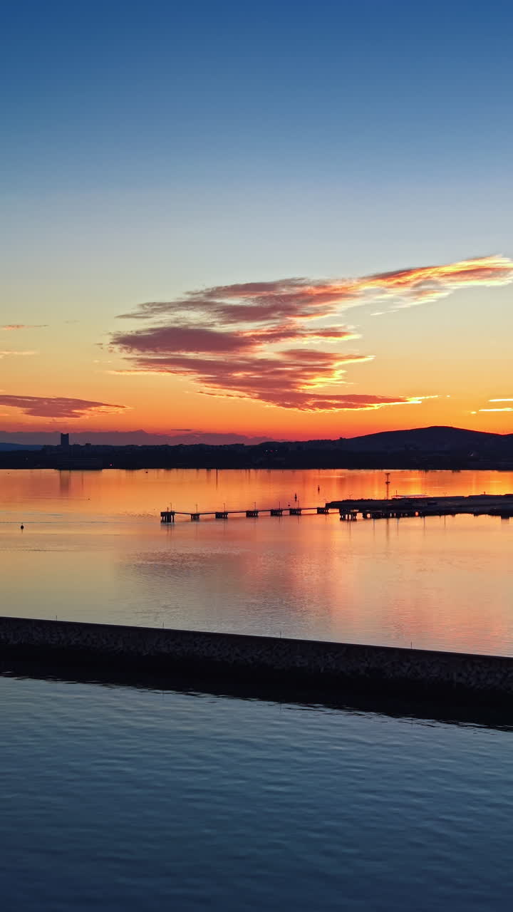 Radiant sunset casts vibrant hues over calm waters and distant silhouettes along the shoreline
