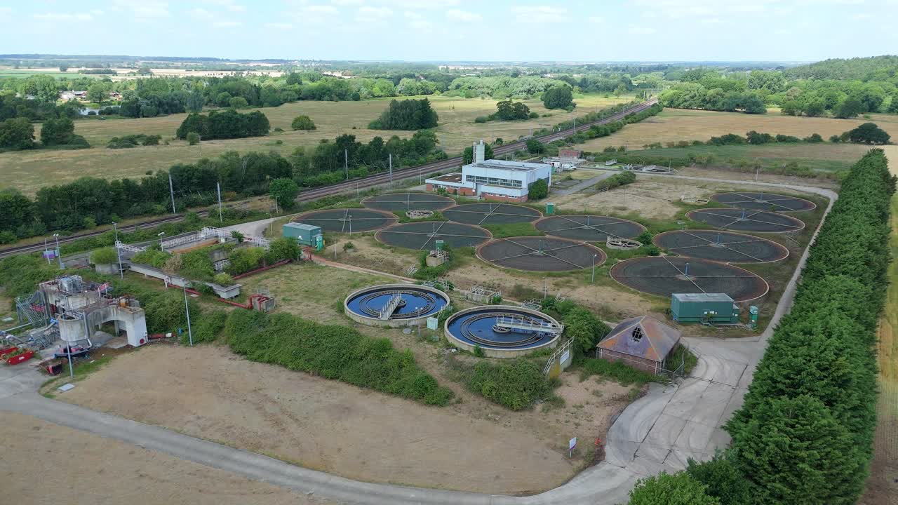 Aerial drone footage of Anglian sewage wastewater treatment plant with filtration tanks and settling pools near train line England
