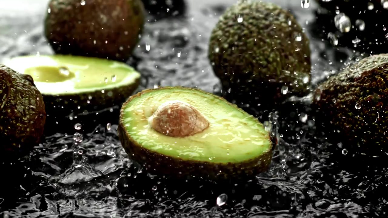 Avocado freschi con schizzi d'acqua su uno sfondo scuro
