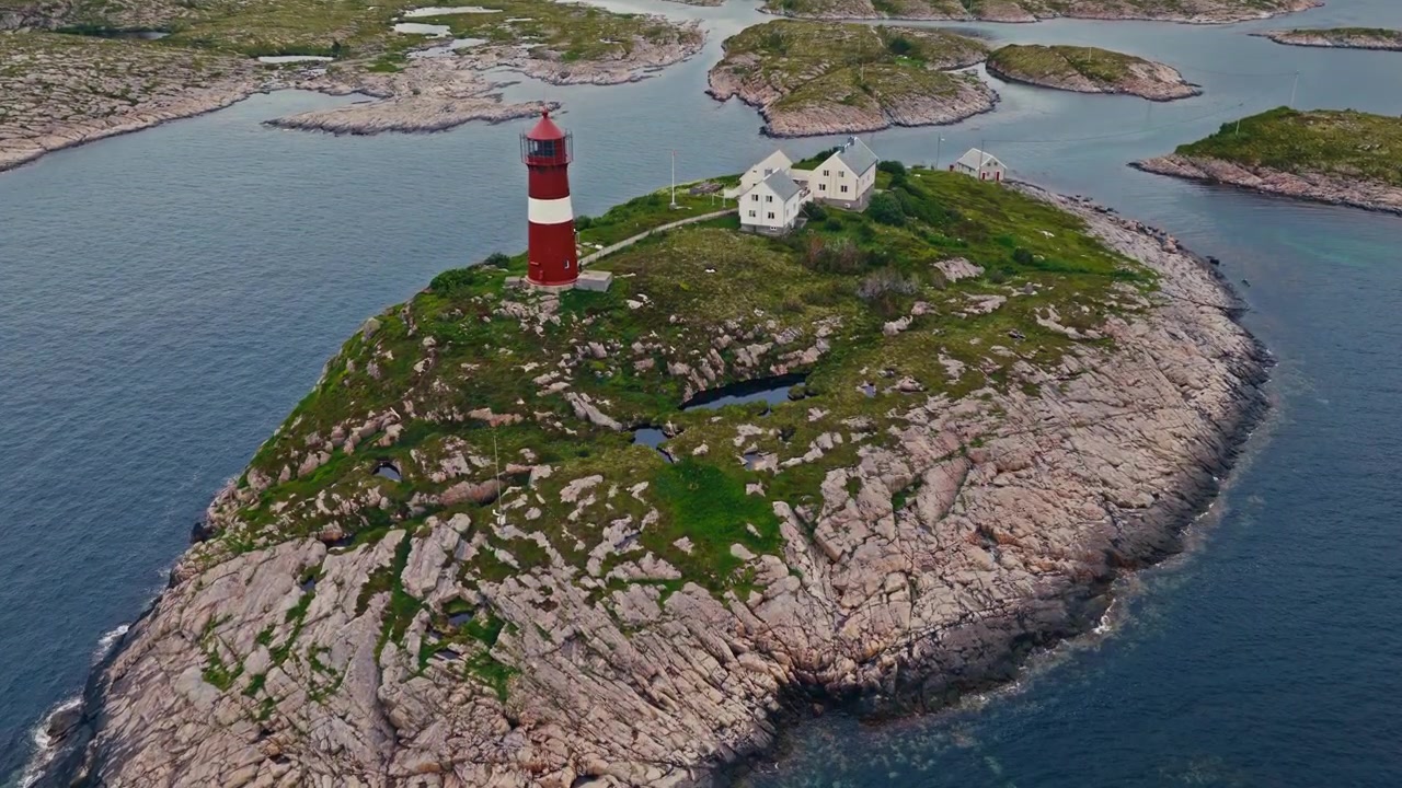 Luftfoto droneudsigt over Buholmrasa Fyr i Trøndelag, Norge, der viser fyrtårnet, den klippefyldte kystlinje, det omkringliggende hav og kystlandskabet.