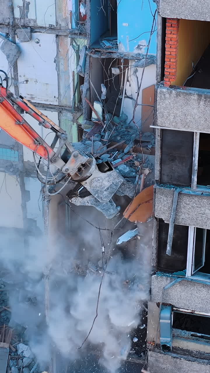 Demolition machine is breaking the floors into pieces and throwing them down. Powerful claw of excavator demolishing the ruined building. Vertical video