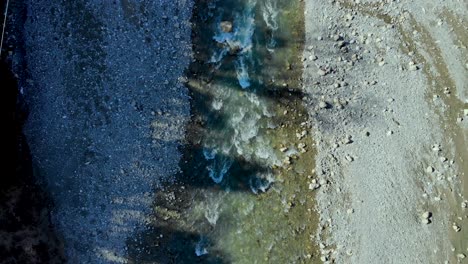 river streaming across pebbles and rocks splashing and foaming, shadow of trees over water surface, top down aerial view