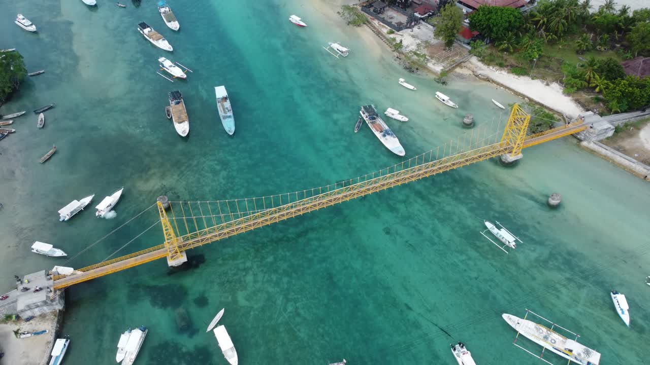 항공 4k 드론 영상: 발리의 누사 렘본간 섬과 누사 세닌간 섬을 연결하는 상징적이고 그림 같은 노란 다리를 가로지르는 스쿠터