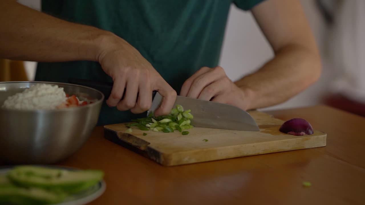 hombre cortando cebolla verde en una tabla de cortar de madera en la cocina de casa