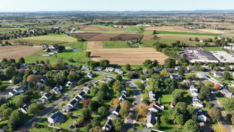 quaint suburb neighborhood of usa with rural farm fields in on bright fall season. modern single family homes and two story buildings. aerial orbit wide shot. new developed housing area of pa,america.