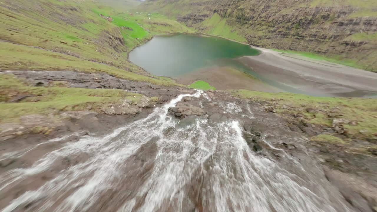 Waterfall flowing into a serene green lake in the faroe islands, aerial view