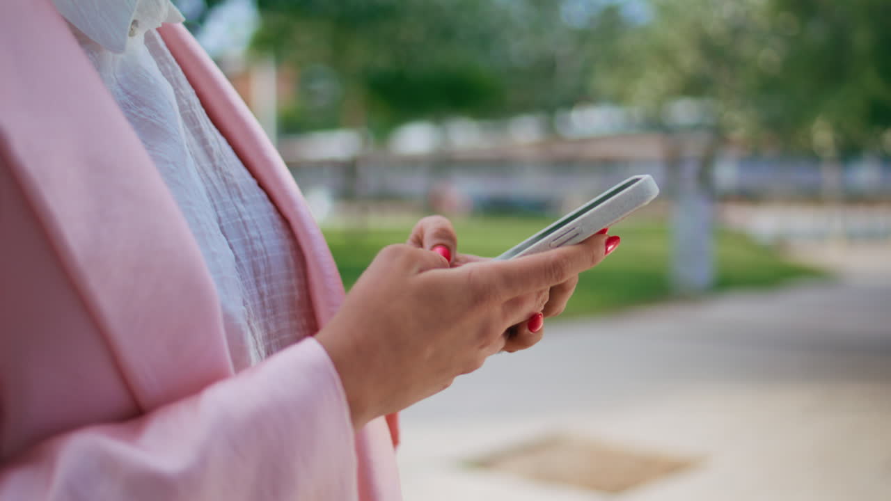 Mani di donna che digitano sullo smartphone per strada, in primo piano. Dita che scrivono sul cellulare.
