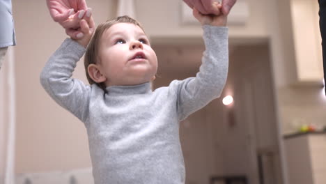 parents holding their baby's hands, helping him take his first steps at home 2