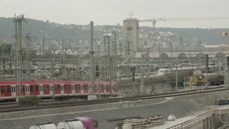 Railway-station-with-multiple-trains-and-tracks,-urban-backdrop-with-industrial-elements,-overcast-sky