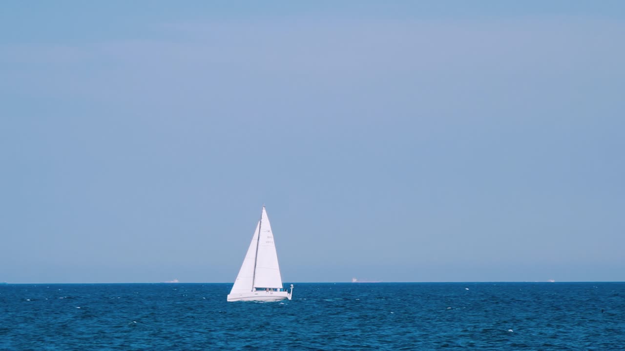 Beautiful white sail on the open sea water. Ship floating alone on the tranquil blue water under the clear sky. Slow motion.
