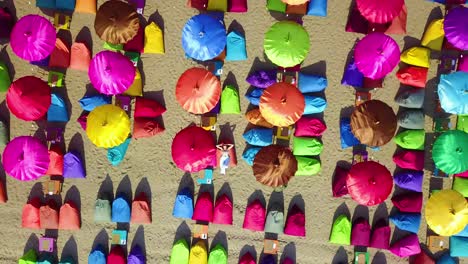 Antena-Sobre-Una-Mujer-Relajarse-Bajo-Coloridas-Sombrillas-En-La-Playa-De-Sanur-O-Kuta-En-La-Costa-De-Bali,-Indonesia