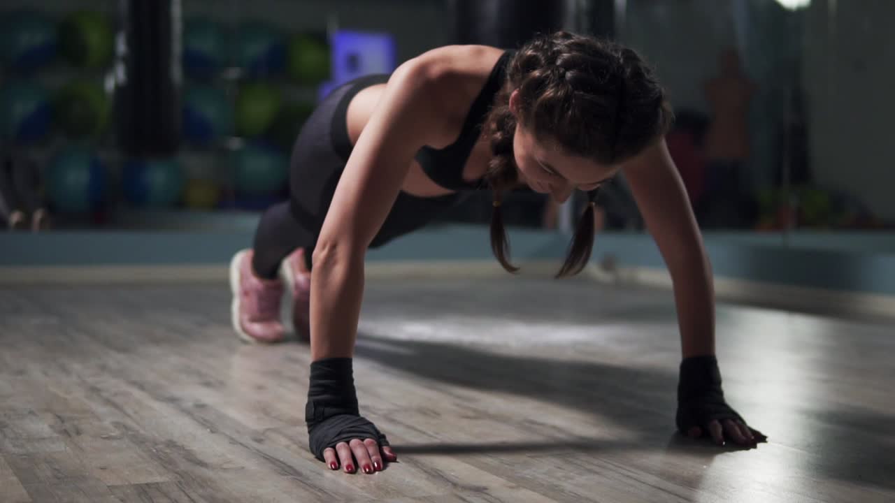 mujer joven haciendo ejercicio de tabla en el gimnasio. mujer de fitness planking con sus manos envueltas en cintas de boxeo, haciendo el peso corporal