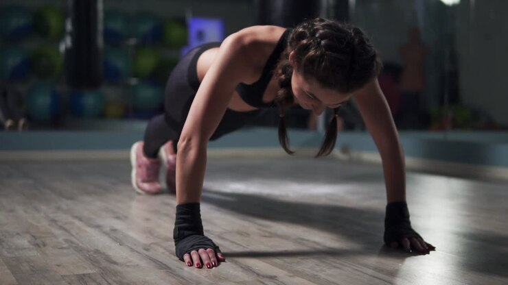 Young woman doing plank exercise in gym. Fitness woman planking with her hands wrapped in boxing tapes, doing the bodyweight