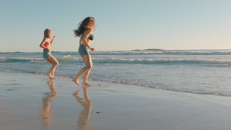 Amigas-Corriendo-En-La-Playa-Hacia-El-Mar-Chapoteando-En-El-Agua-Divirtiéndose-Jugando-Adolescentes-Disfrutando-De-Un-Cálido-Día-De-Verano-En-Vacaciones