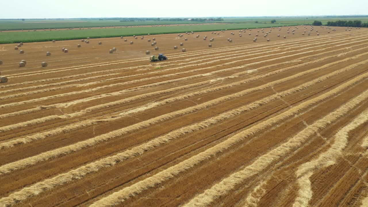 Aerial circling view of tractor tow trailed bale machine to collect straw from harvested field