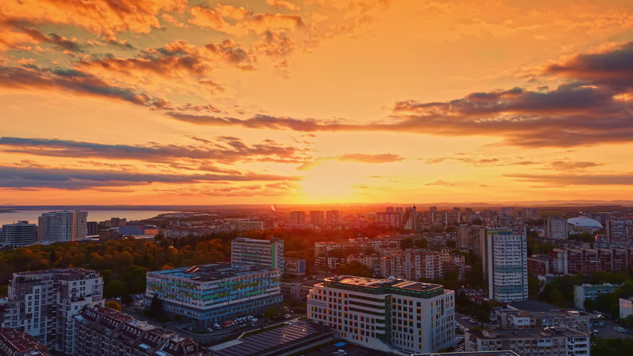 Pôr do sol sobre uma cidade com edifícios e nuvens ao fundo, exibindo um céu colorido no final do dia, visto de um ponto alto da cidade ao entardecer