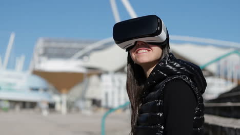 Young-dark-haired-woman-in-warm-black-waistcoat-wearing-virtual-reality-glasses-turning-head-to-camera