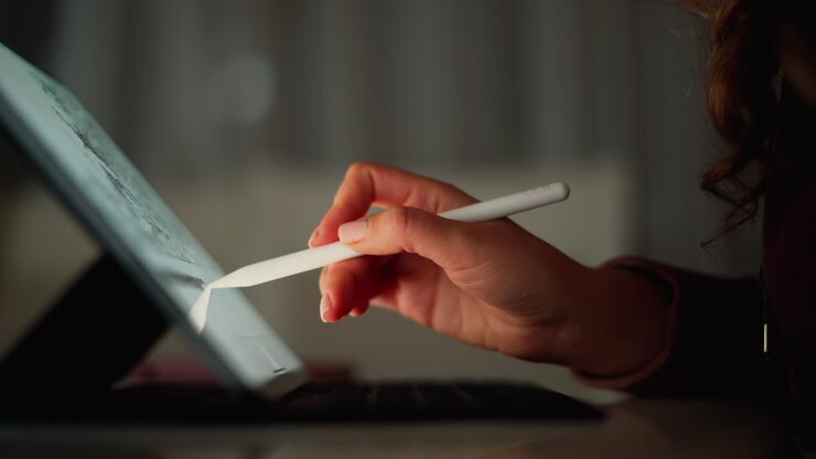 Nahaufnahme einer Frau, die abends mit einem Stift auf einem Tablet zeichnet