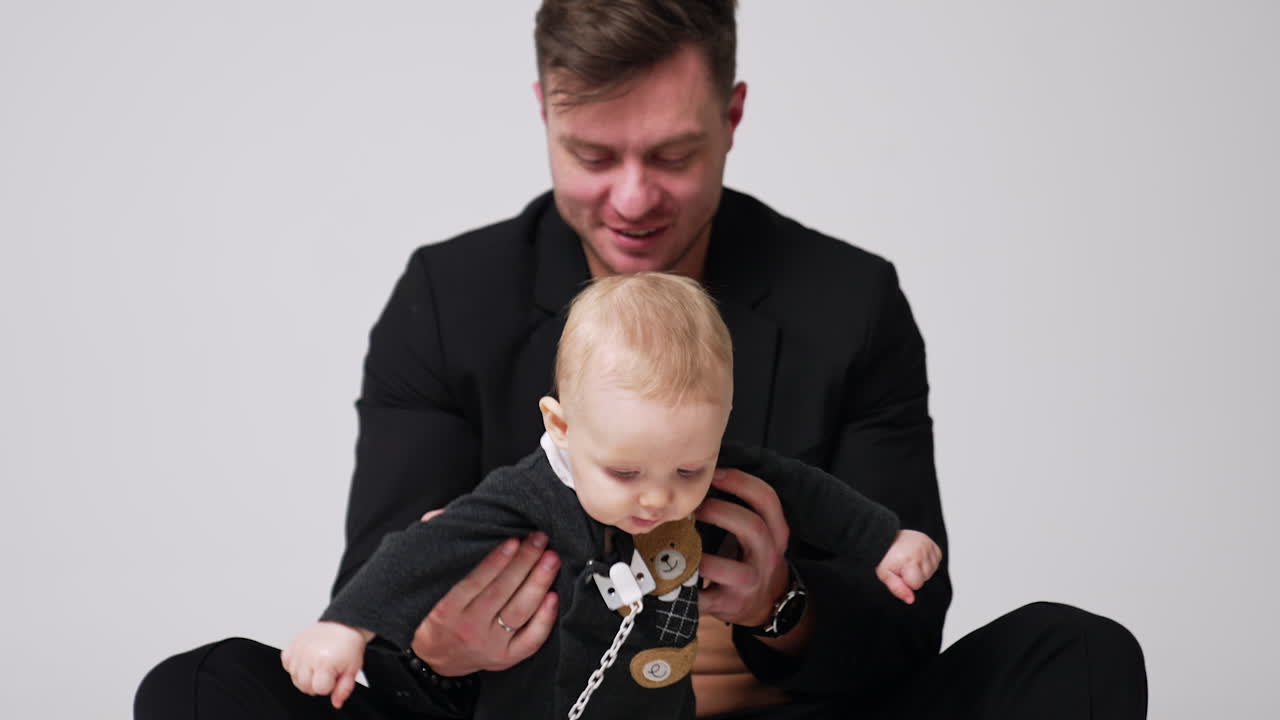 Loving father kisses his beloved baby. Happy dad with a little son starting to walk. White backdrop.
