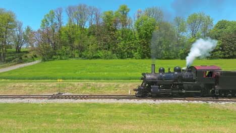 una vista lateral de un antiguo tren de pasajeros de vapor que comienza a moverse lentamente, soplando humo negro en un día soleado de primavera