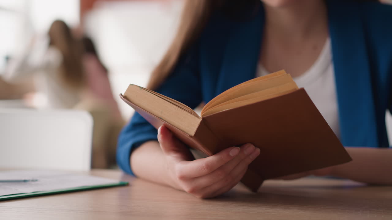 한 여성이 도서관에서 오래된 책 페이지를 뒤집고 있습니다. 정식 재을 입은 여자는 대학에서 책상에서 빈티지 소설을 읽습니다. 방문자는 에세이를 위해 문학을 사용합니다.