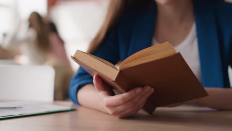 una mujer da la vuelta a las páginas de un libro viejo en un primer plano de la biblioteca. una dama con una chaqueta formal lee una novela antigua en el escritorio de la universidad. un visitante trabaja con literatura para un ensayo
