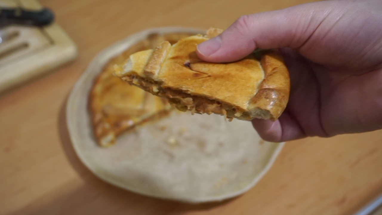 Close-up of a person holding a freshly baked slice of a savory tuna empanada over a wooden table