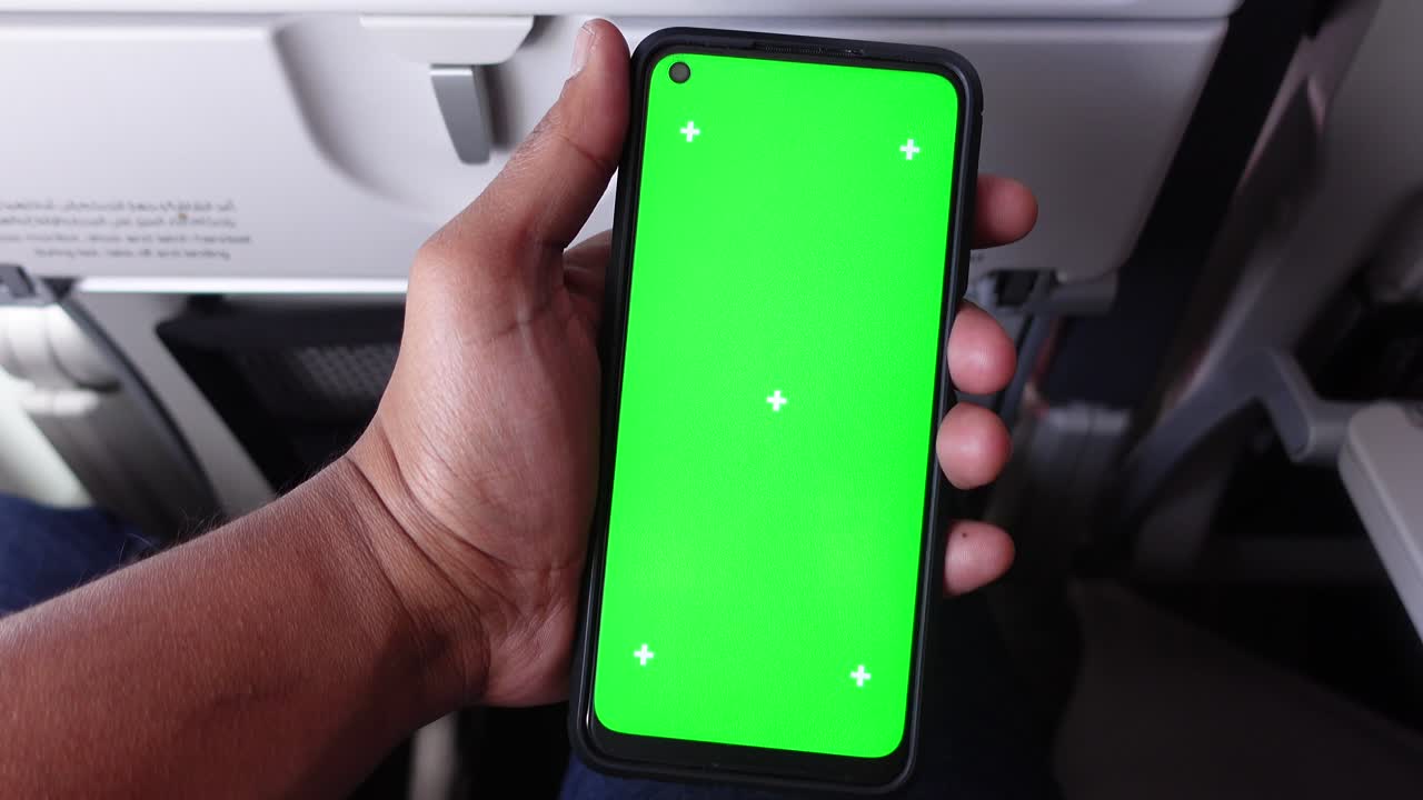 mano sosteniendo un teléfono inteligente con pantalla verde en el avión