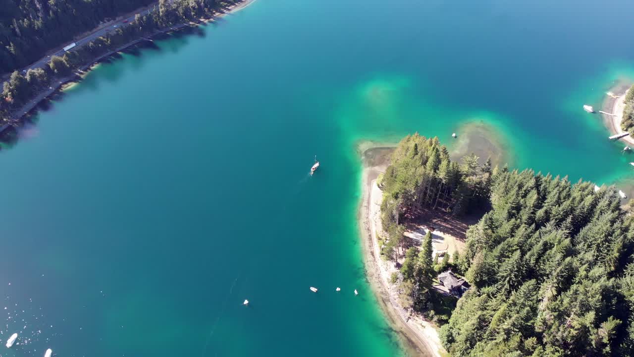 Aerial descends as sailboat motors around point in clear blue lake
