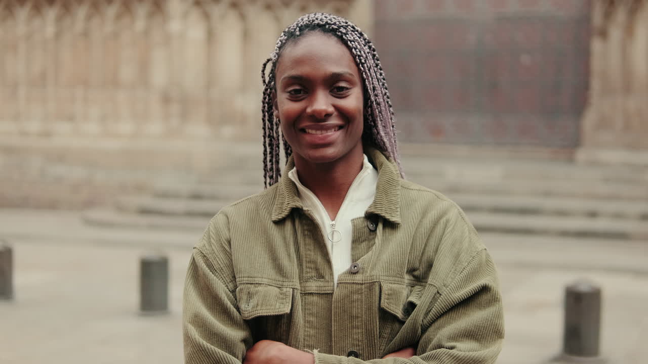 Jeune femme noire avec des tresses souriant à la caméra en extérieur
