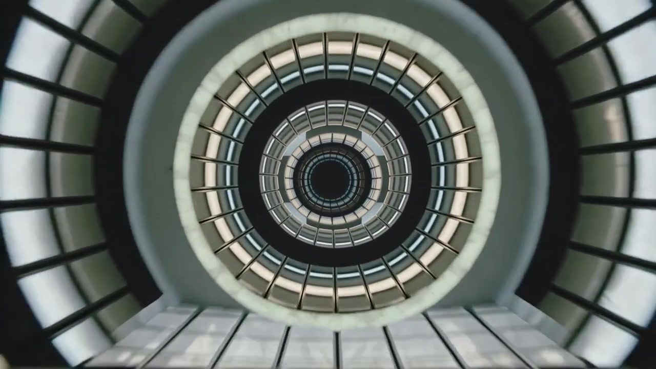 Eine sich bewegende Kamera fährt durch einen Atriumschacht im Inneren eines Gebäudes und enthüllt konzentrische Ringe und ein Oberlicht.